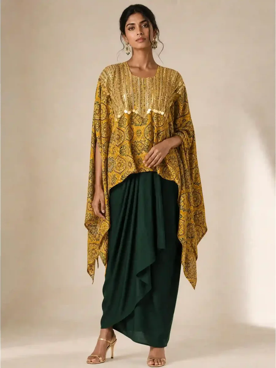 Model wearing a loose mustard paisley kaftan-style top with gold embellishments and a dark green draped skirt.